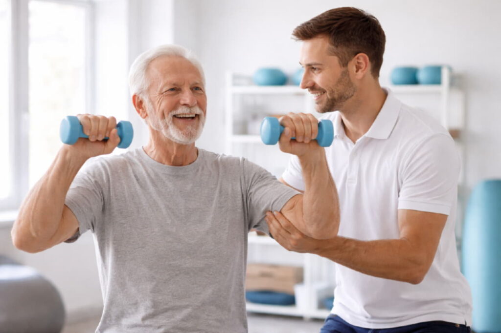 Пожилой человек выполняет силовые упражнения с лёгкими гантелями под наблюдением специалиста