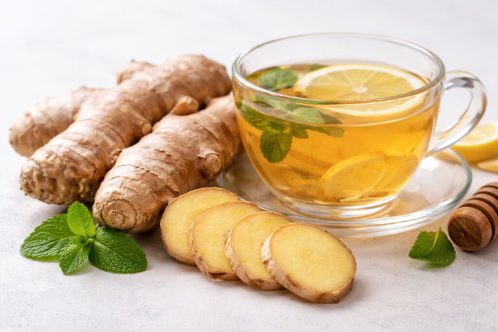 Свежий корень имбиря и нарезанные ломтики рядом с чашкой имбирного чая