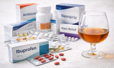 Таблетки ибупрофена рядом с упаковками разных лекарств и бокалом алкоголя